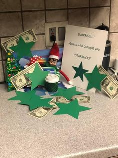 the elf is sitting on the counter next to money and a sign that says surprise i guess who brought you starbuck's