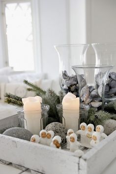 some candles are sitting in a tray with rocks and pine cones on the table next to them