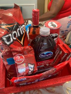 a basket filled with drinks and snacks on top of a table next to a woman