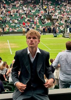 a man in a suit sitting on a bench at a tennis match