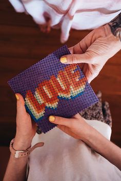 a woman holding up a piece of beaded fabric with the word love spelled on it