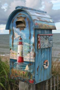 a blue mailbox with a painting of a lighthouse on it's side next to the ocean