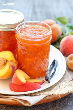 two jars filled with peach jam sitting on top of a white plate next to sliced peaches