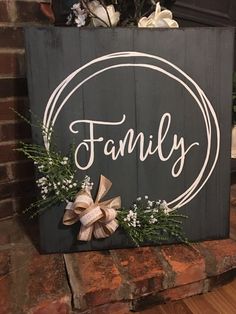 a sign that says family on it with flowers and greenery in front of a brick wall