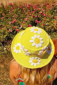 a woman wearing a yellow hat with flowers on it sitting in front of a flower garden