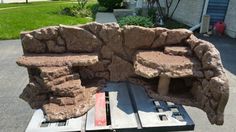 an outdoor bench made out of rocks sitting on a pallet in front of a house