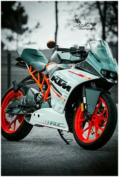 an orange and white motorcycle parked on the street with trees in the backgroud