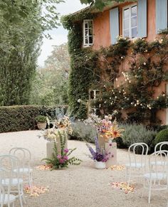 an outdoor ceremony with white chairs and flowers on the ground in front of a building