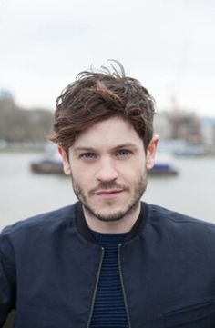 a man standing in front of a body of water wearing a blue shirt and black jacket