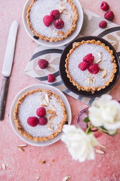 three small pies with raspberries on top are sitting on a pink table