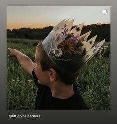 a young boy wearing a paper crown on top of his head in the middle of a field