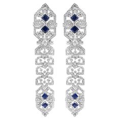 Stunning 18 karat white gold earrings adorned with diamonds and blue sapphires. The intricate design showcases a symmetrical pattern with princess-cut blue sapphires set in the centre, surrounded by sparkling diamonds. The geometric detailing adds a unique and luxurious touch, making these earrings a perfect statement piece for any elegant occasion. Diamond Total Weight: 6.4 carats All Mozafarian jewellery comes with a valuation certificate. Luxury White Gold Diamond Earrings With Intricate Design, Symmetrical Pattern, White Gold Earrings, Diamond Drops, Diamond Drop Earrings, Sapphire Diamond, Sparkle Diamonds, Showcase Design, Princess Cut