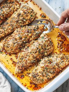 a person scooping chicken into a casserole dish with cheese and herbs on top