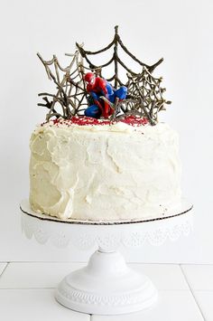 a spiderman cake with white frosting and sprinkles sits on a pedestal