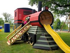 a child is playing on a slide in the park with a train shaped structure behind it