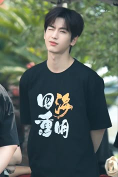 a young man standing in front of a tree wearing a black t - shirt with an orange dragon on it