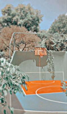 the basketball court is painted orange and blue with trees in the backgrouds