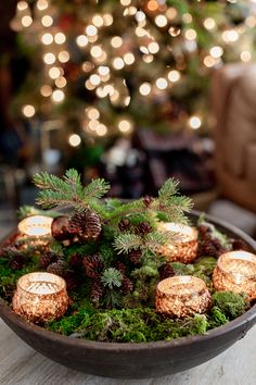 a wooden bowl filled with pine cones and candles on top of a table next to a christmas tree