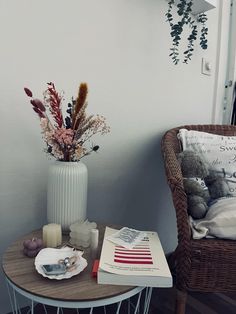 a white vase with flowers on top of a table next to a chair and book