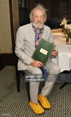 an older man sitting at a table with a book in his hand and wearing yellow shoes