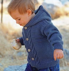 a young boy holding a donut and wearing a blue sweater while standing on a rock