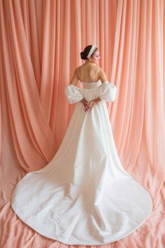 a woman in a white dress is posing for the camera with pink curtains behind her