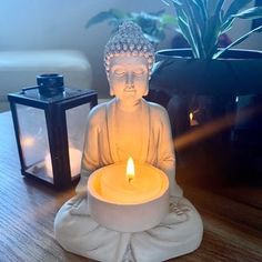 a buddha statue sitting on top of a wooden table next to a candle and potted plant