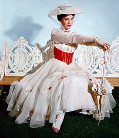 a woman sitting on a bench wearing a dress and hat with flowers in her hair