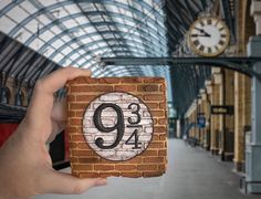 a person holding up a brick block with the number nine on it in front of a train station