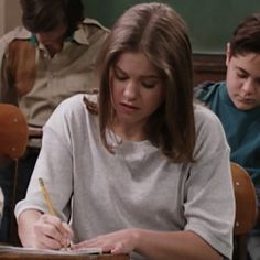 a woman sitting at a desk writing in front of two other people and holding a pen