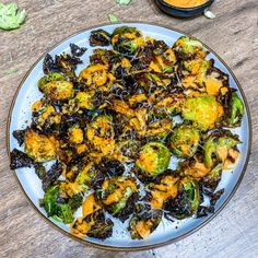 a white plate topped with broccoli covered in sauce next to a bowl of dip