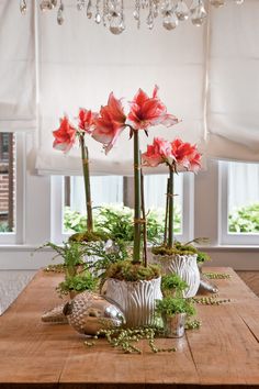 three red flowers in silver vases on a wooden table with greenery and crystal chandelier