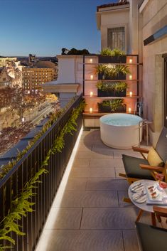 a balcony with a hot tub and chairs on it, overlooking the city at night