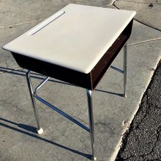 a white table sitting on top of a sidewalk next to a parking lot with no one around it