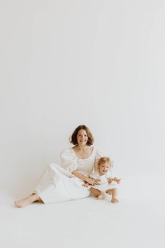 a mother and her baby sitting on the floor in white clothes with their arms around each other