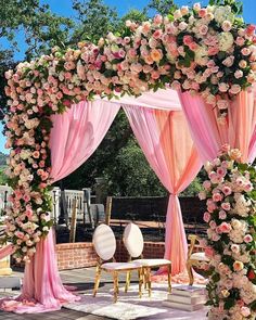 an outdoor wedding ceremony with pink and white flowers on the arch, draping