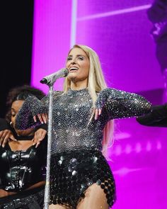 a woman in a black and silver outfit singing into a microphone