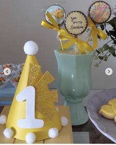 a blue vase filled with yellow and white cake pops next to a number one cupcake