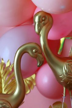 two gold flamingos standing next to each other in front of pink and white balloons