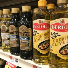 several bottles of cooking olive oil on a shelf in a grocery store, with price tags below