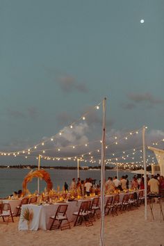 a long table set up on the beach with lights strung over it for an event