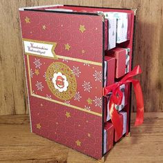 an open red book with gold trim and ribbon tied around the edges, sitting on a wooden surface