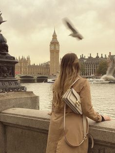 a woman is looking out over the water at a bird flying in front of her