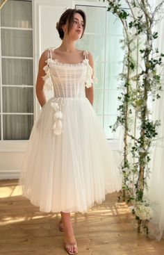 a woman standing in front of a window wearing a white dress with flowers on it