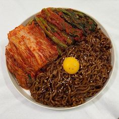 a white plate topped with noodles and meat next to an egg on top of it