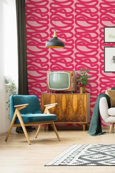 a living room with pink and green wallpaper, two chairs, a tv and a rug on the floor