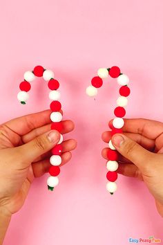 two hands holding candy beads forming the word love on a pink background with white and red balls