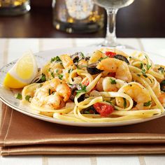 a plate of pasta with shrimp, mushrooms and lemon wedges next to a glass of wine