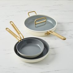 two pots and pans with gold handles sitting on a marble countertop next to each other