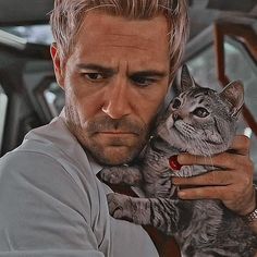 a man holding a cat in his right hand and looking at the camera with an intense look on his face